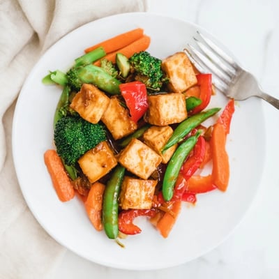 Savory Spring Vegetable Stir Fry with Tofu served hot over steamed rice, garnished with toasted sesame seeds.