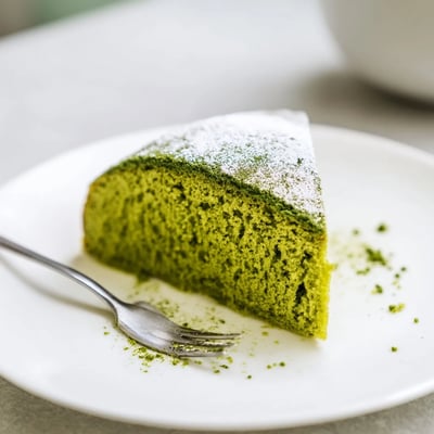 Warm matcha cake recipe topped with a sweet powdered sugar glaze, surrounded by scattered fresh berries.